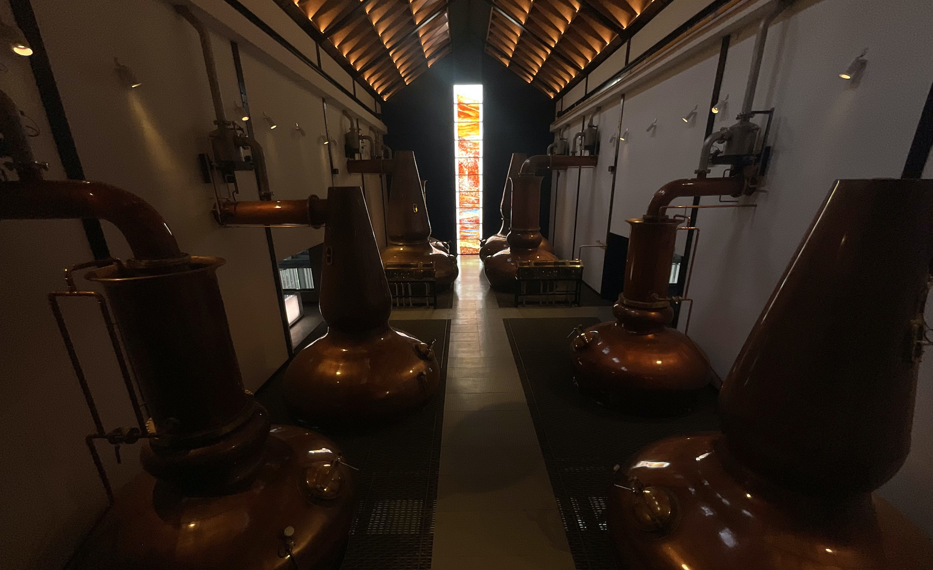 Das Dalmore Brennhaus — vier Paare von Kupferbrennblasen mit dem leuchtenden Fusionsglasfenster am Ende, Alness, Schottland