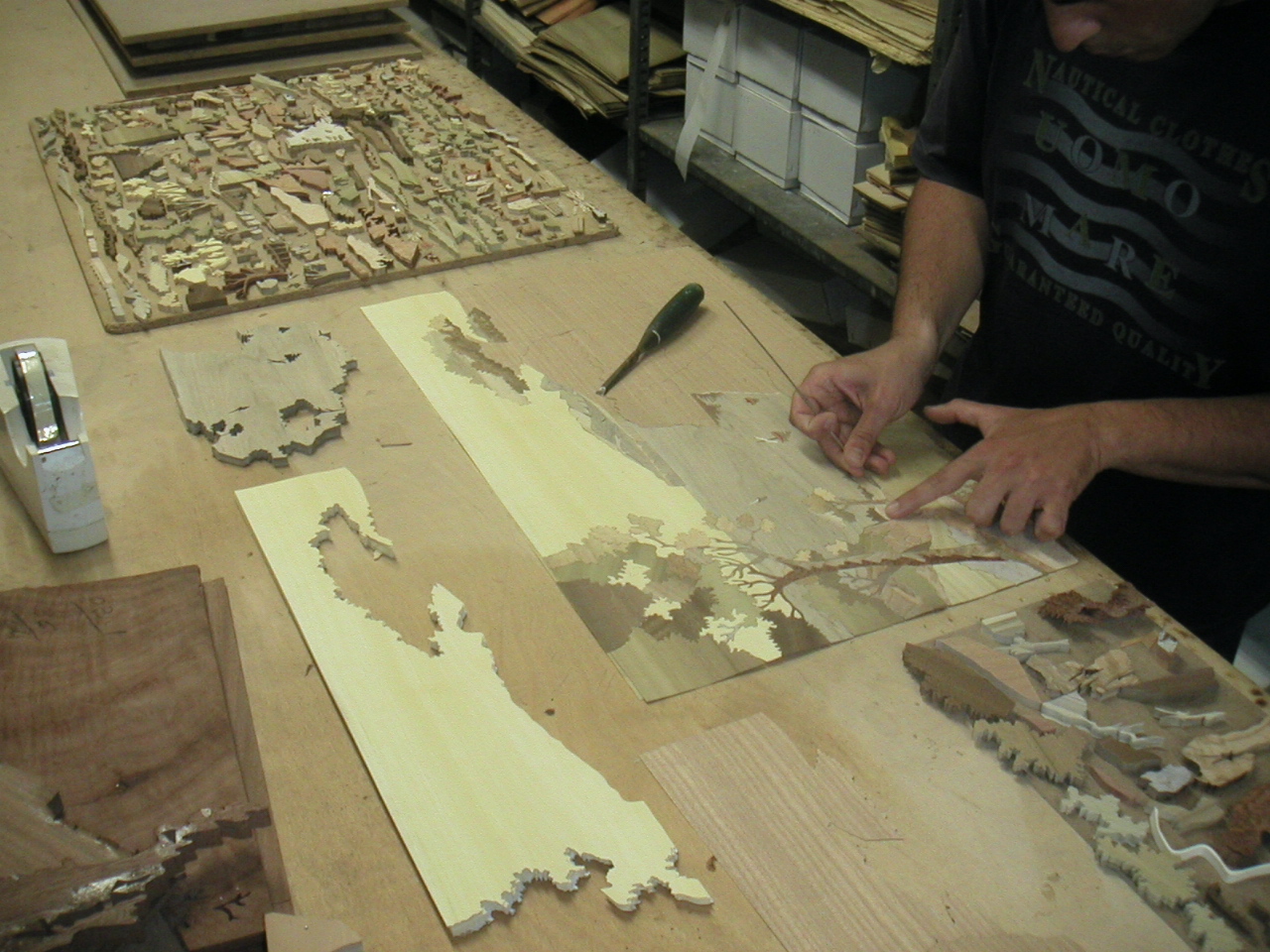 Sorrento workshop — landscape panels being assembled, tray of city scene pieces in background showing multiple-copy production